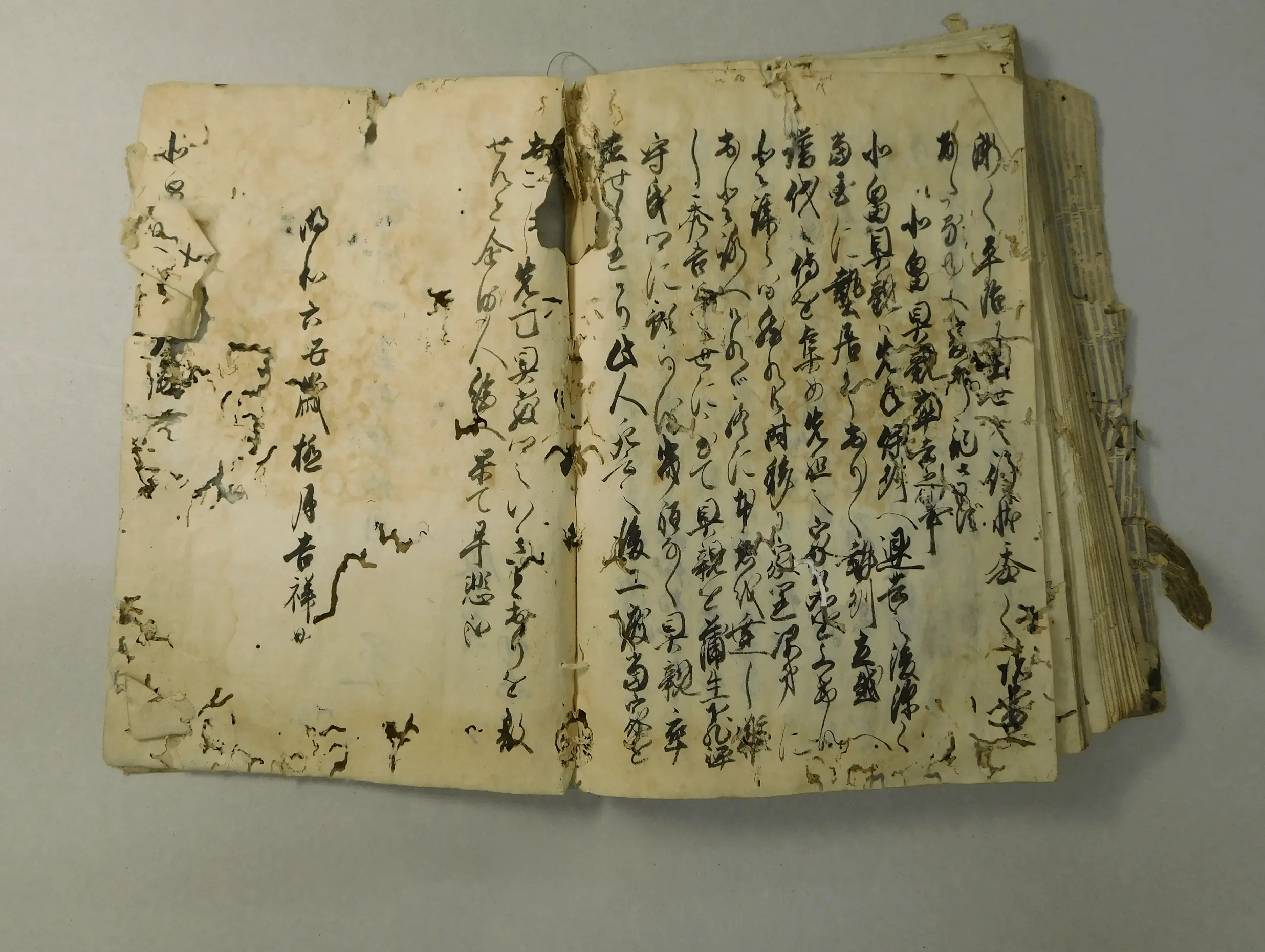 虫損や破れ、紙の欠損、シミや変色が広範囲に見られる修復前の古文書の見開きページで、文字の判読が難しく資料の劣化が進行している状態。三重県伊勢市の株式会社辻村表具店が修復を担当する前の古文書修復事例