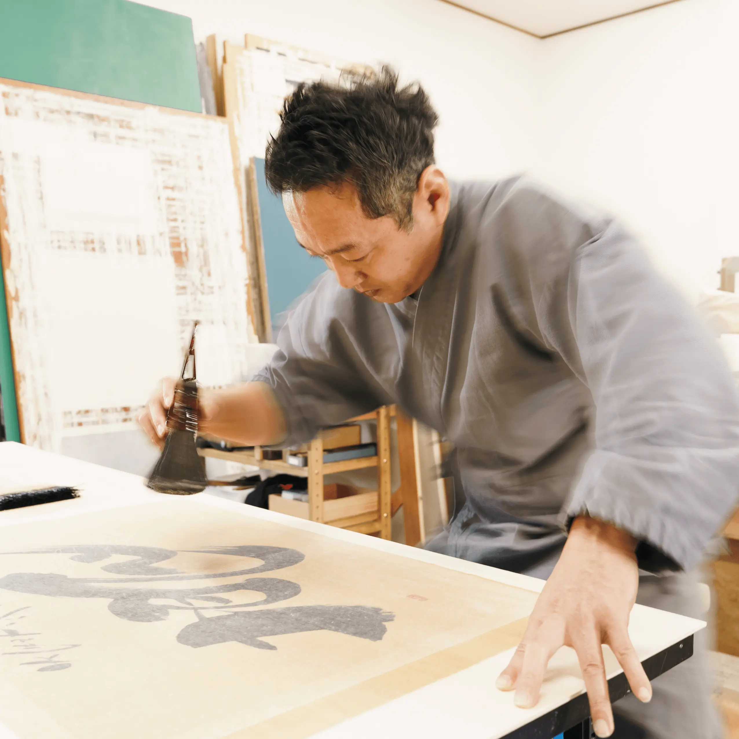 大きな筆を使って掛け軸の書き付けを行っている表具師の作業風景。伝統技法による掛け軸修復と表装を行う三重県伊勢市の株式会社辻村表具店の職人仕事