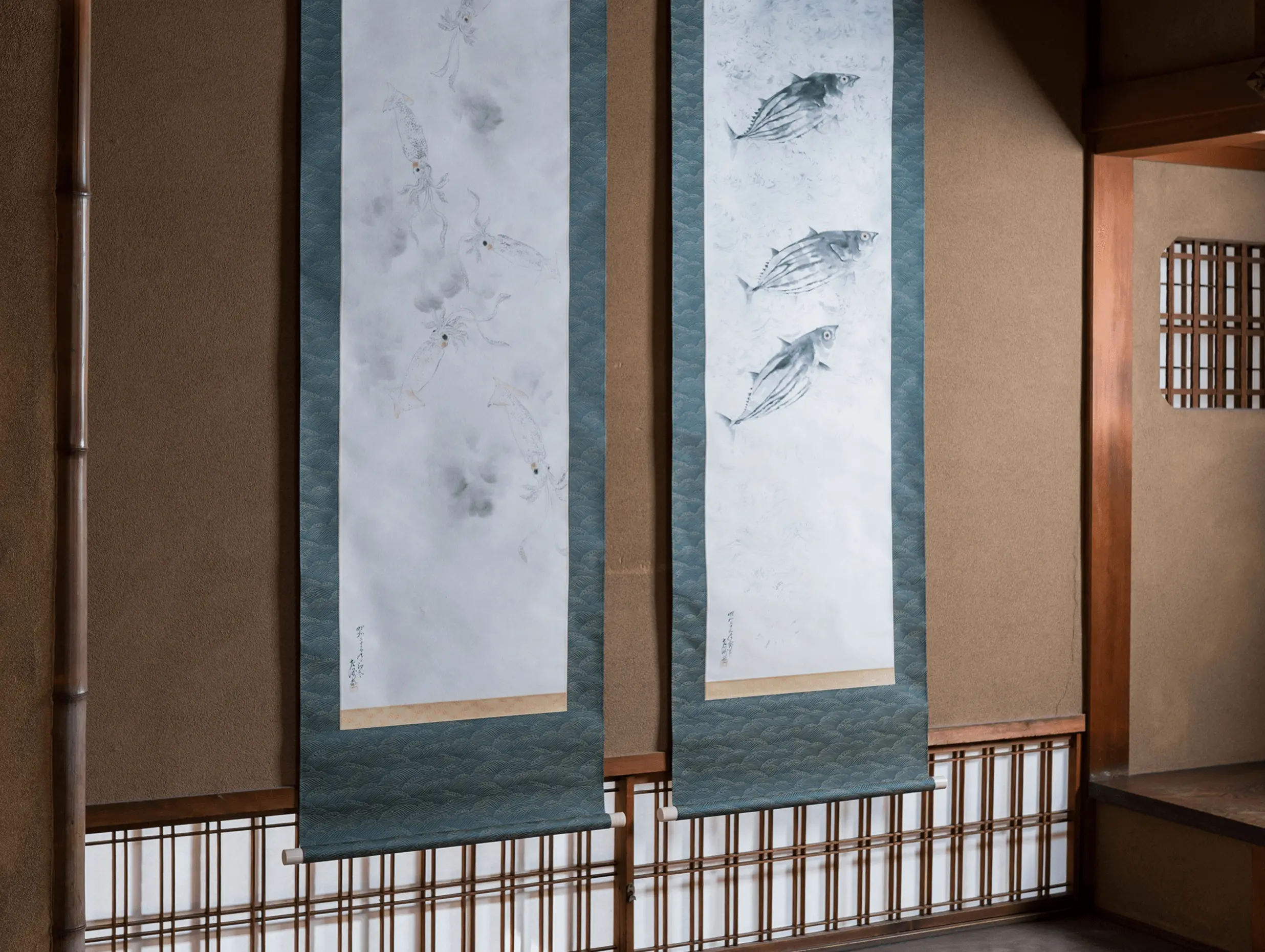 和室の床の間に並べて掛けられた2幅の掛け軸で、魚と烏賊を描いた日本画作品の展示風景。掛け軸修復と表装を行う三重県伊勢市の株式会社辻村表具店による仕立て事例