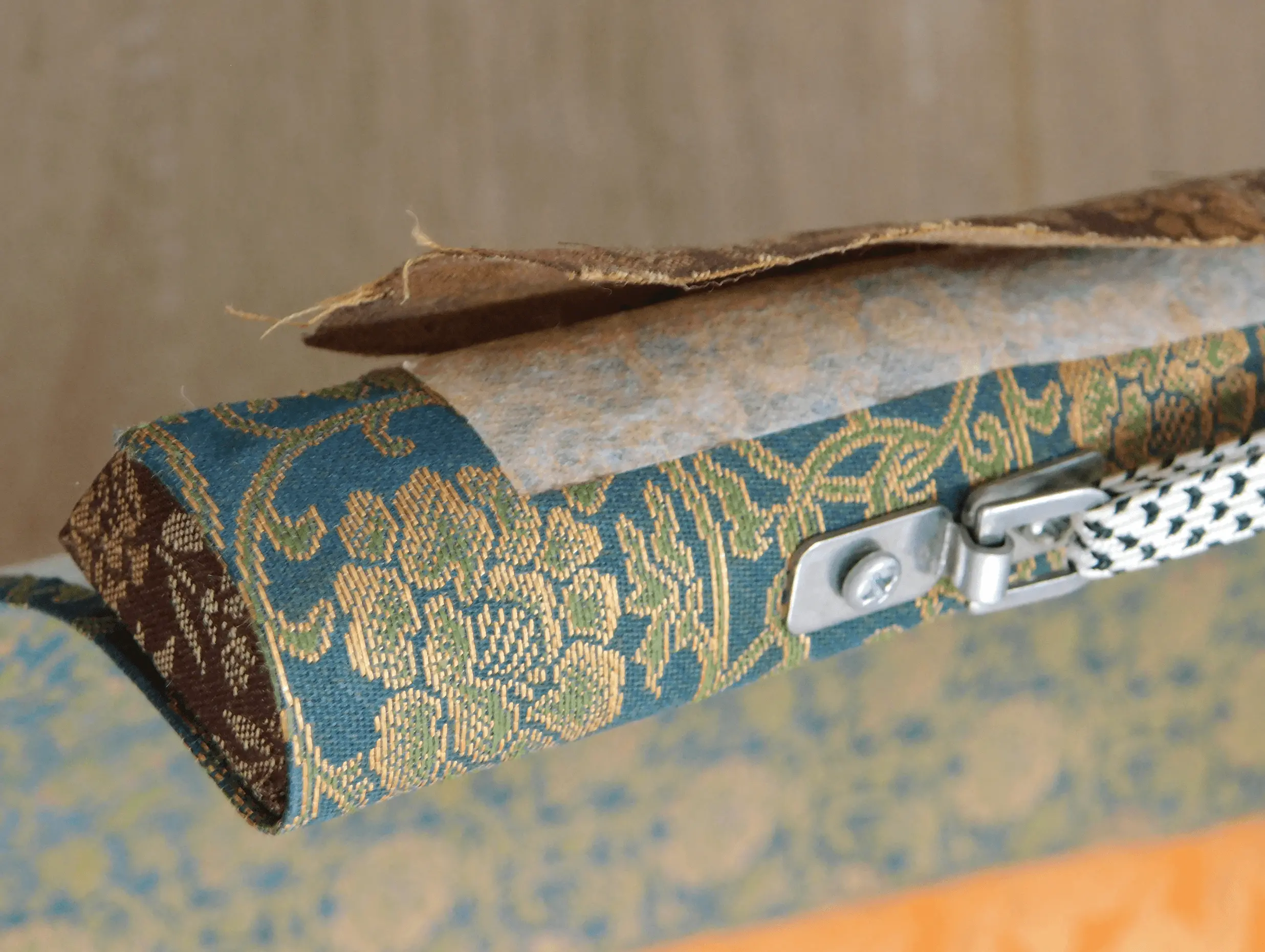 掛け軸の上部の軸先と裂地部分の拡大で、経年劣化した布や裏紙が浮き上がっている修復前の状態。三重県伊勢市の株式会社辻村表具店が対応する掛け軸修復工程の一部