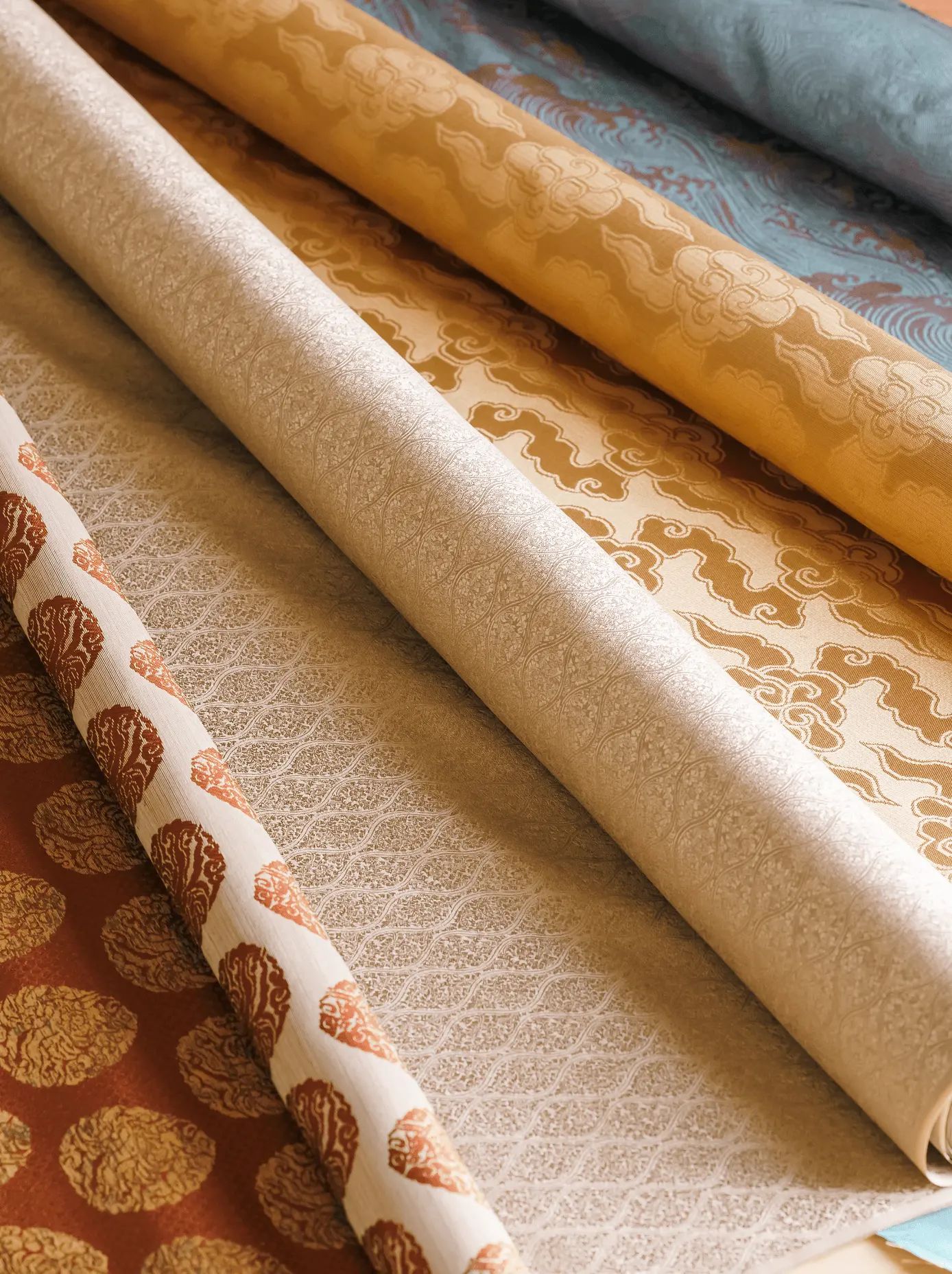 表装に使用する金襴や裂地など複数種類の反物を並べた様子で、掛け軸の仕立てや修復に用いる伝統的な布地の見本。三重県伊勢市の株式会社辻村表具店の表装材料