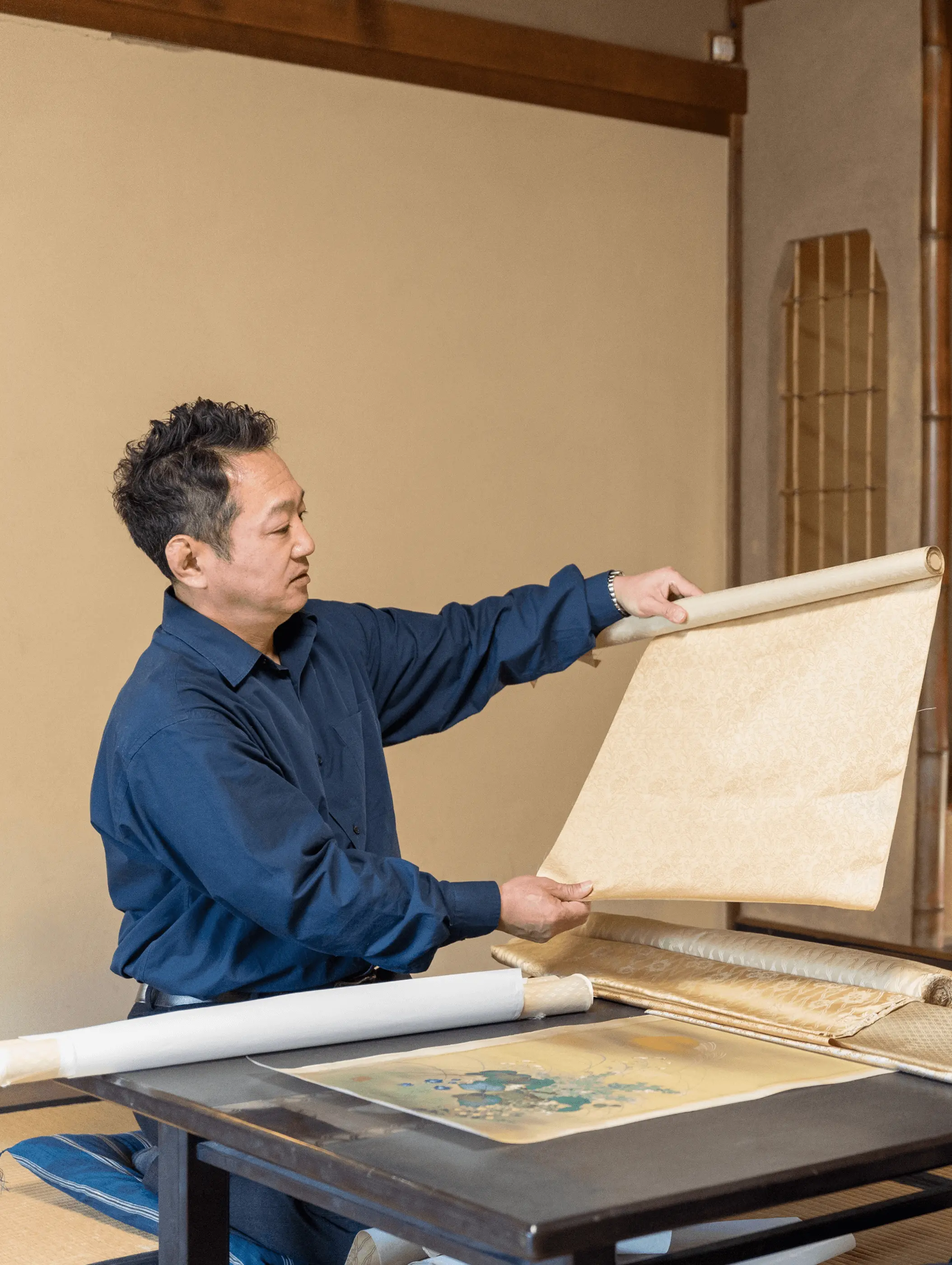 掛け軸の本紙の上に裏打ち用の和紙を重ね、空気を抜きながら手で丁寧に貼り合わせている表装作業の様子。株式会社辻村表具店（三重県伊勢市）による掛け軸修復工程