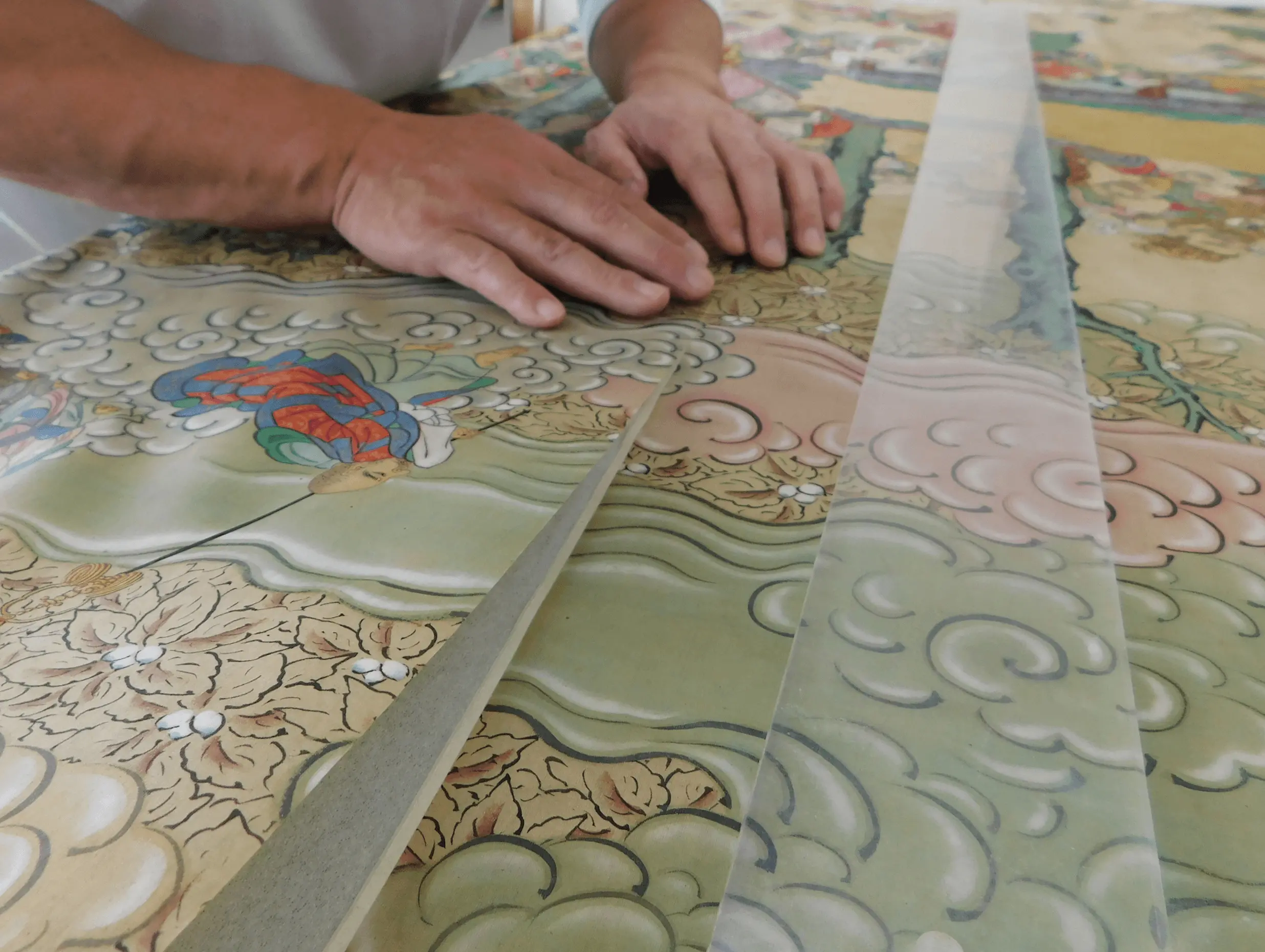 作業台の上で掛け軸用の裂地を広げ、色味や柄のバランスを確認している表具師の様子。掛け軸修復と新調表装を行う三重県伊勢市の株式会社辻村表具店の制作風景