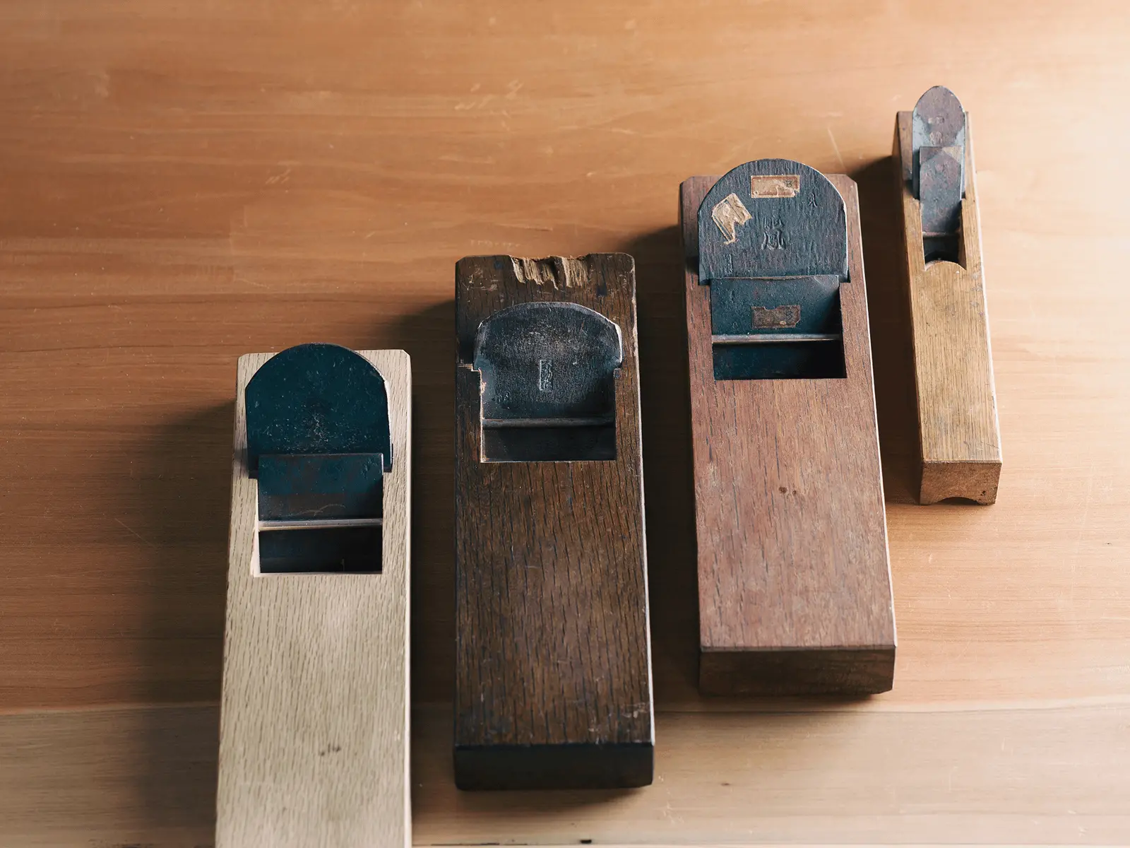 大きさの異なる木製の鉋（かんな）が作業台の上に横一列に並べられており、表具師が掛け軸や木地の調整に使用する伝統工具の種類が分かる