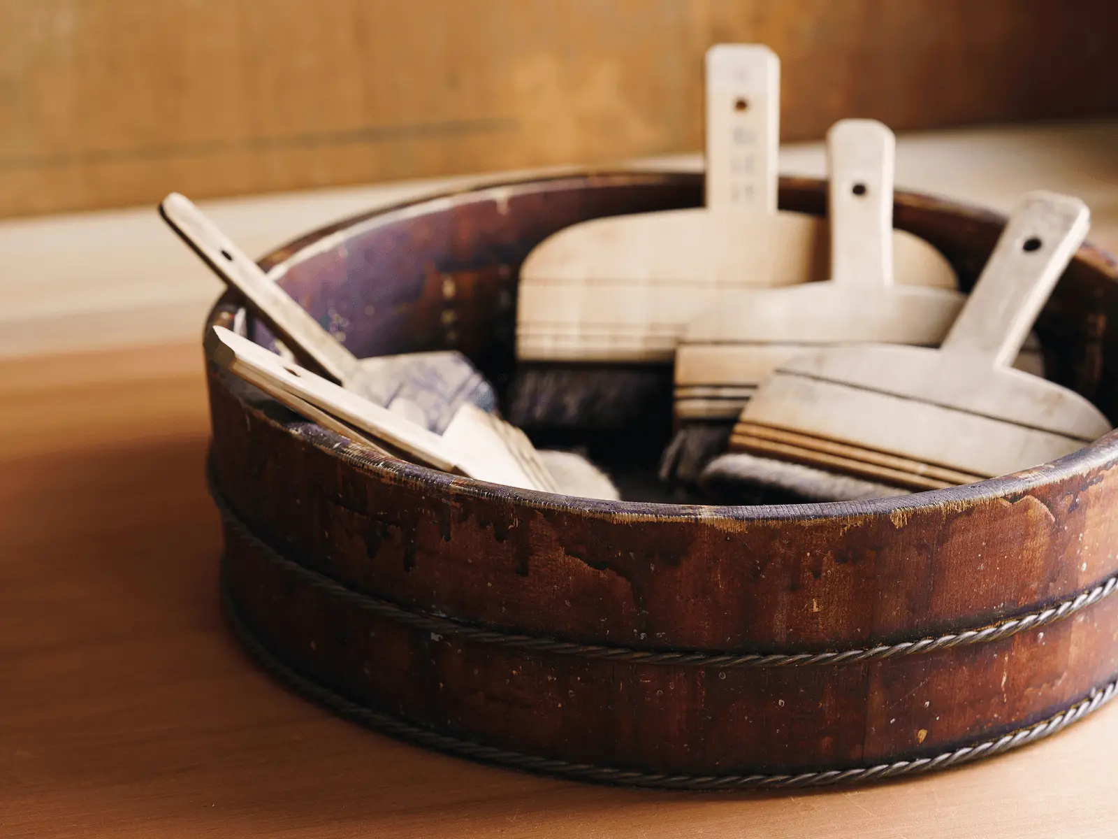 木桶の中に数本の裏打ち用刷毛が入れられて保管されており、表具工房で掛け軸や古文書修復に用いる道具を実際の作業環境で管理している様子