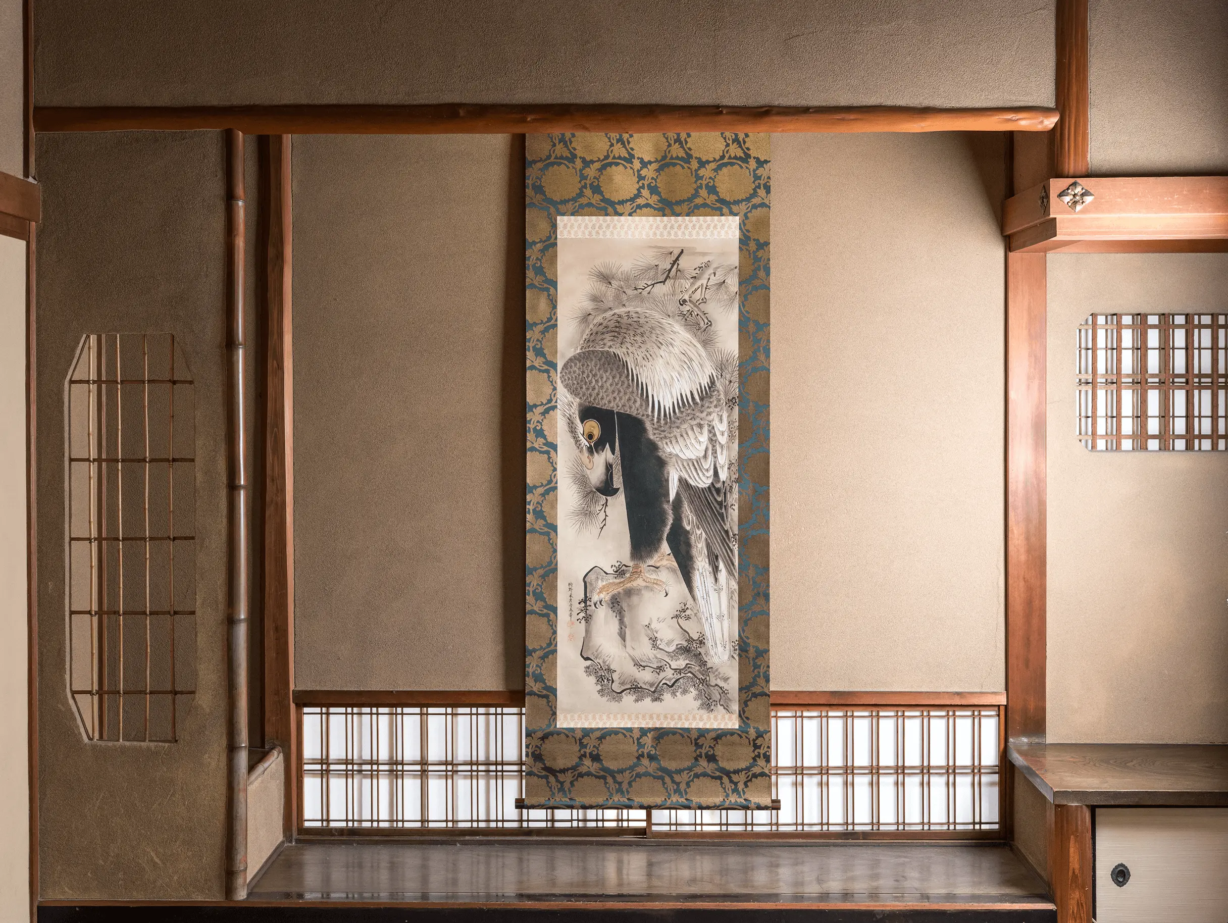 和室の床の間に展示された鷹の図柄の掛け軸。精緻な筆致で描かれた鷹と金襴裂地の表装が特徴で、掛け軸修復や文化財修復の完成例を示している。''