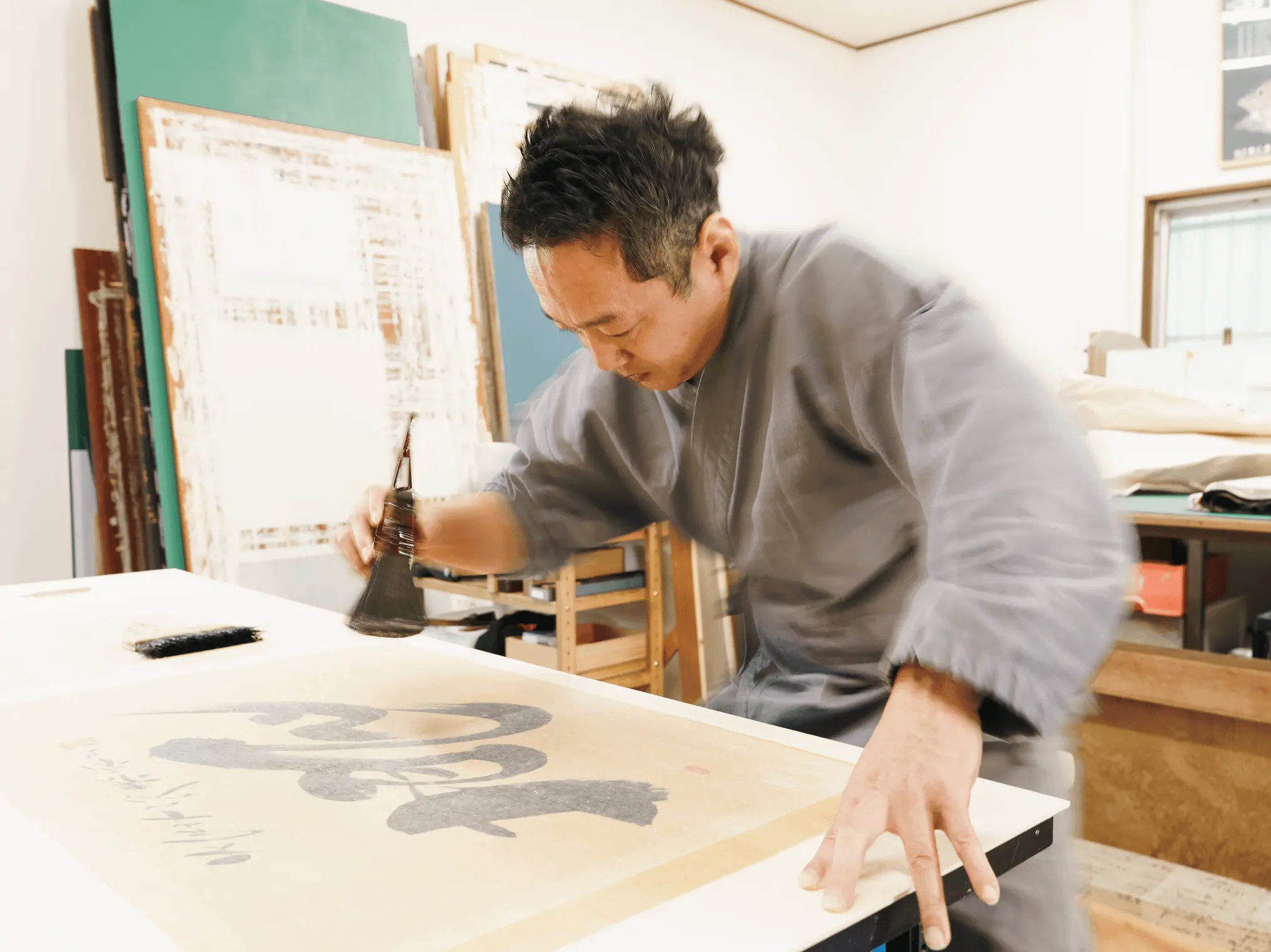 表具師が工房で掛け軸の書画部分を刷毛を使って修復している作業風景。裏打ちや補修工程の様子が分かり、掛け軸修復と伝統的な表装技術の専門性を伝える。