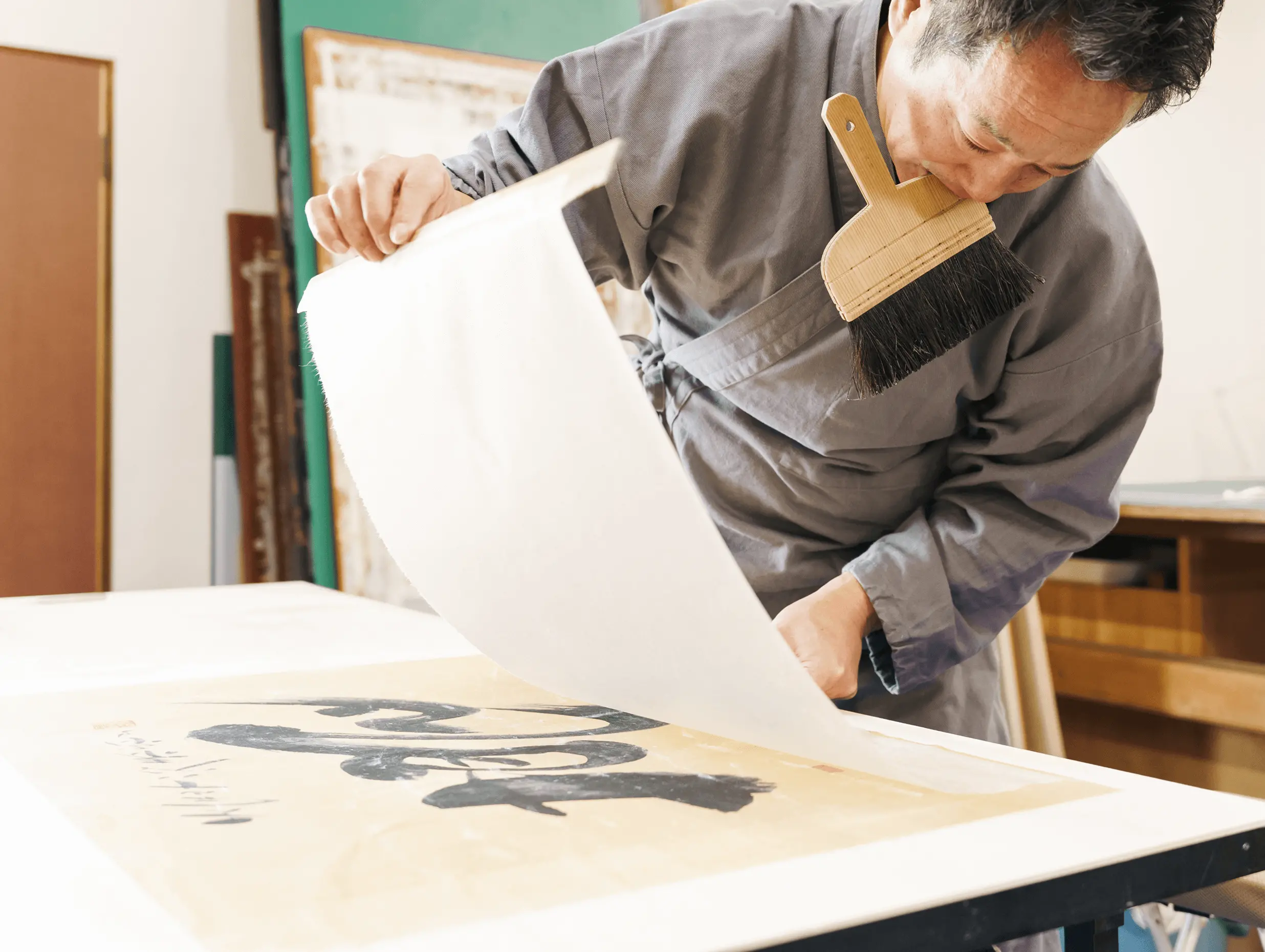 表具師が刷毛を使いながら、書画作品の上に新しい和紙を重ねて仕上げ作業を行っている様子。掛け軸や古書の修復後の仕立て工程で、長期保存と美観を両立させる伝統技法。