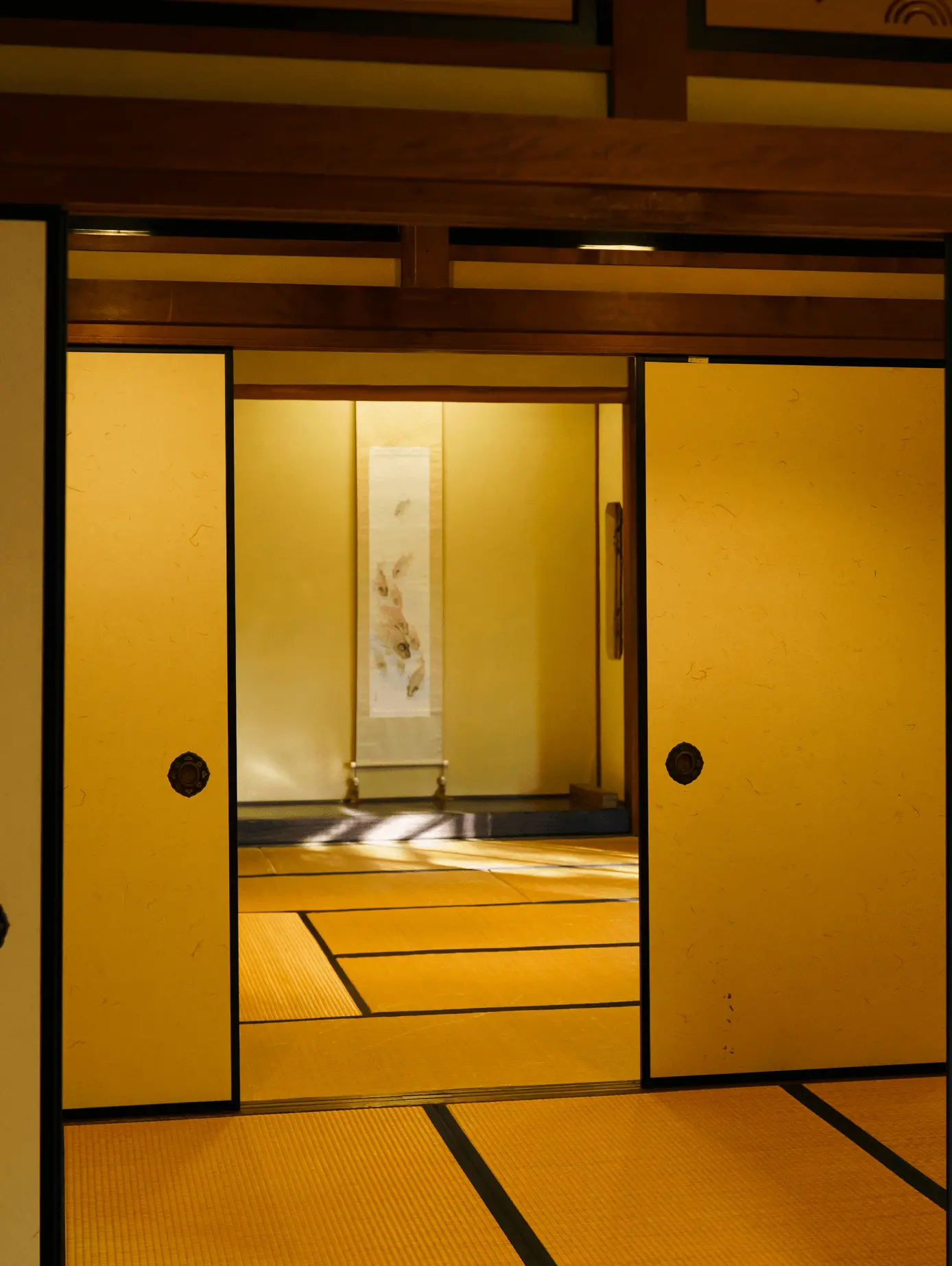 襖を開けた先に床の間と掛け軸が見える伝統的な和室の室内写真。修復された襖と畳、木組み天井が調和し、襖修理・障子張替え・和室改修による日本住宅の美しい空間演出を表している。