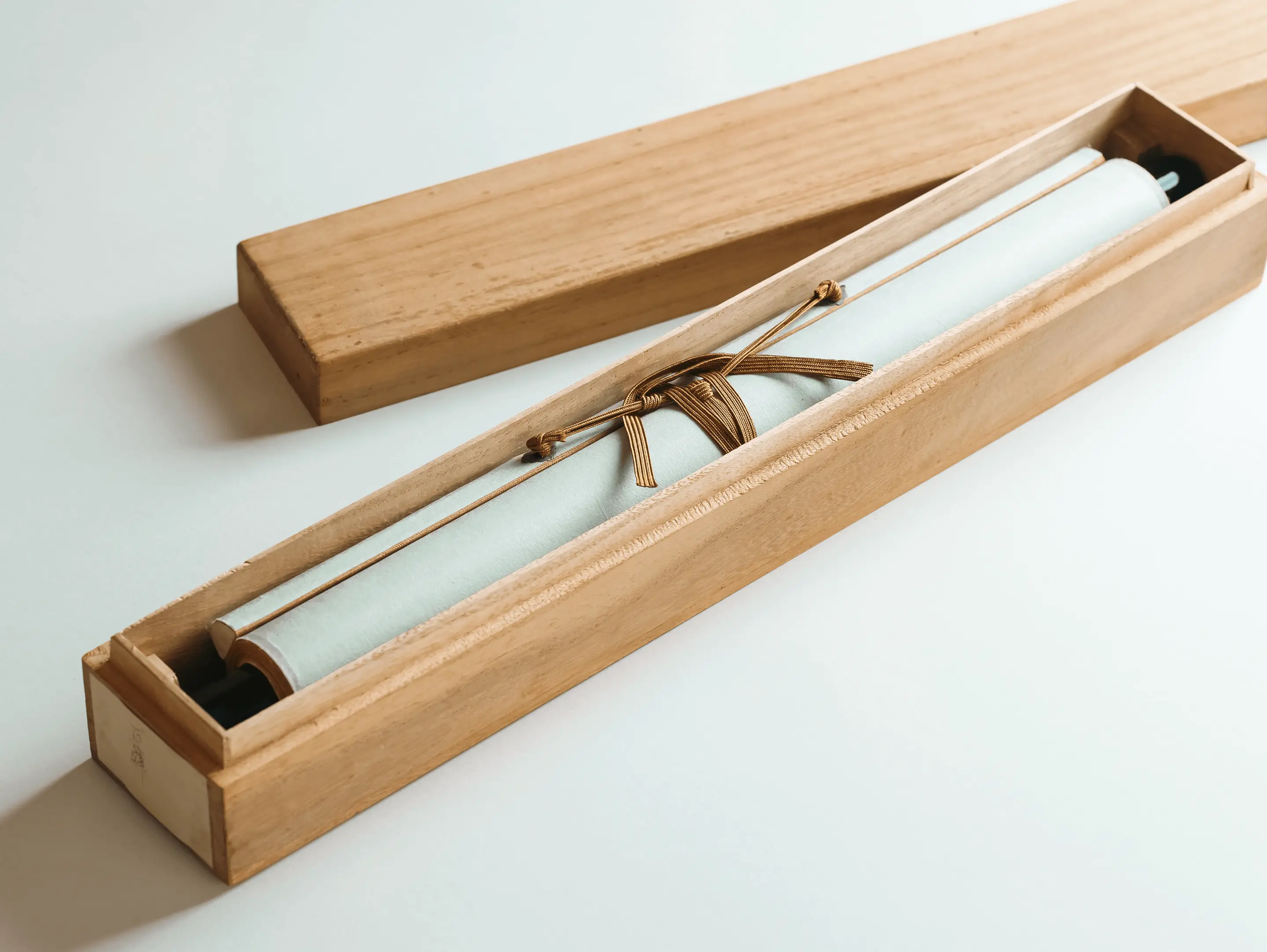 桐箱に収納された掛け軸の保管状態。薄い青緑色の布で包まれた掛け軸が専用の木製桐箱に納められ、金色の組紐で結ばれている伊勢市辻村表具店の適切な保管方法
