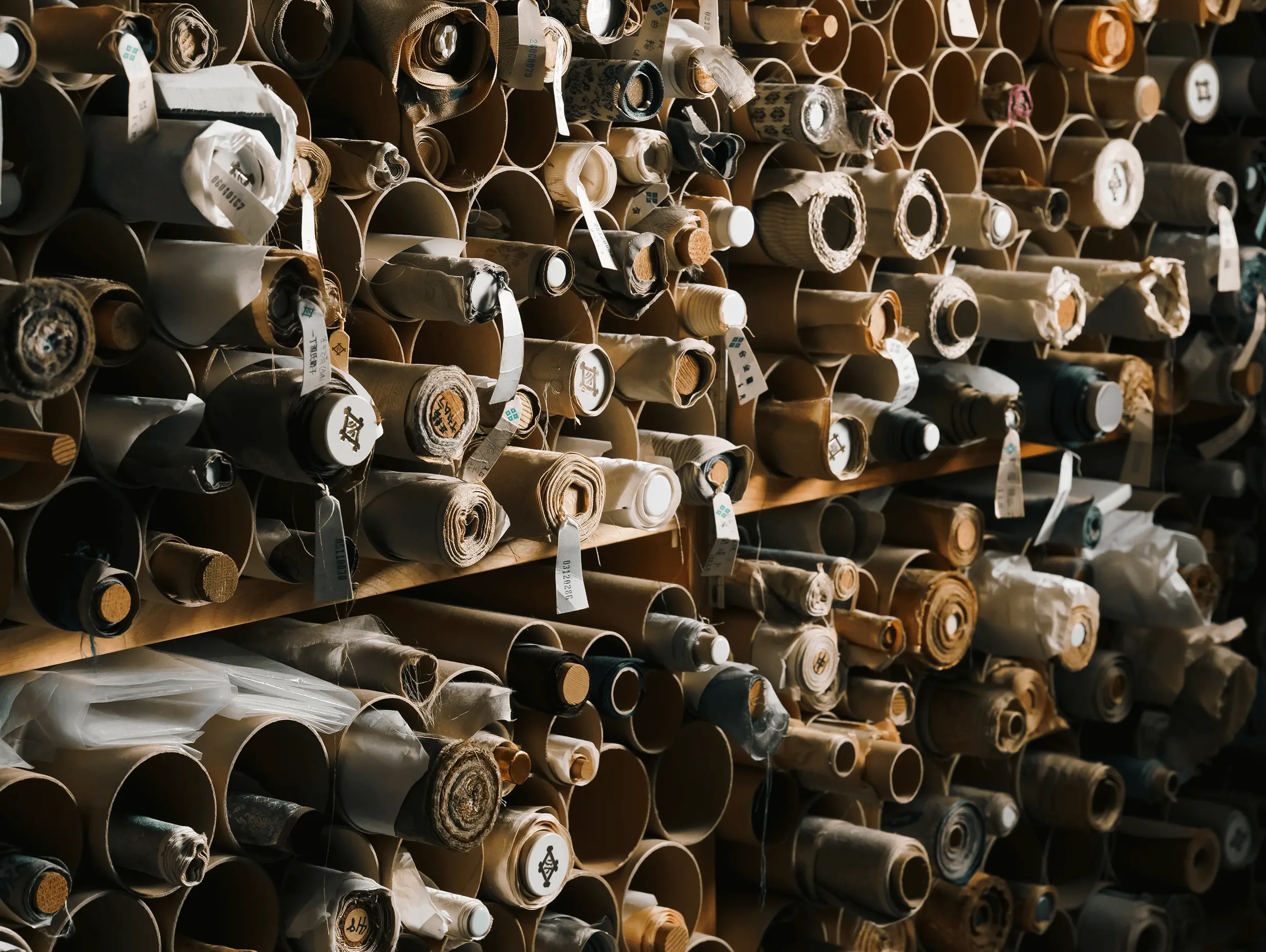 株式会社辻村表具店（三重県伊勢市）の工房で、掛け軸や襖の表装・修復に使用する裂地や和紙を紙管に巻いて大量に保管している様子で、素材の種類や管理体制が分かる